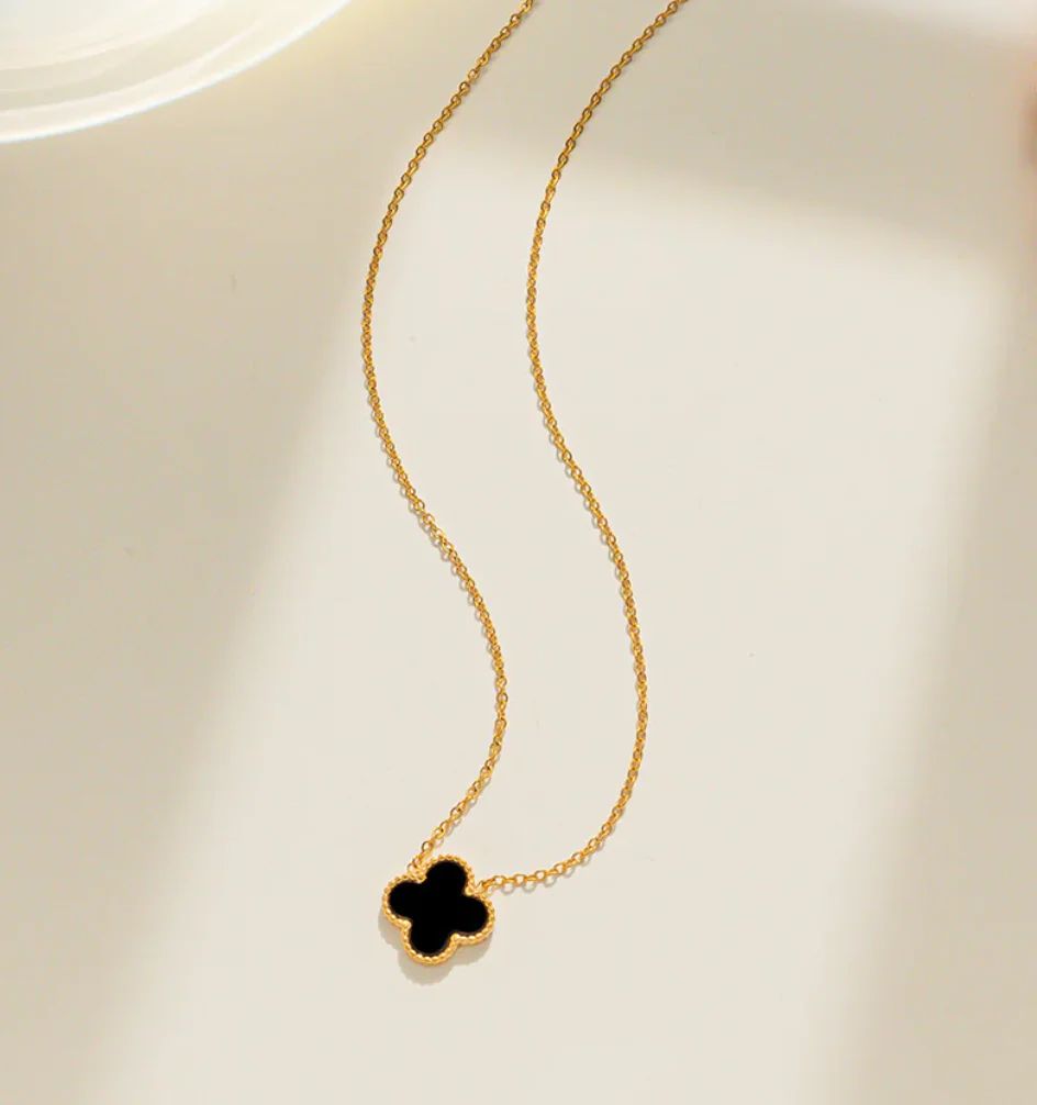 Gold stainless steel necklace with black four-leaf clover pendant on a light background