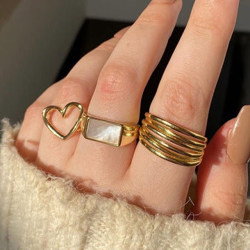 Woman's hand wearing multiple gold rings with heart, mother-of-pearl, and stacked band designs