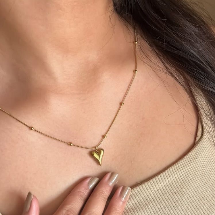 Gold stainless steel necklace with heart pendant and bead accents on a neutral background