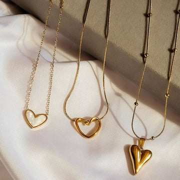 Three gold heart pendant necklaces on white silk fabric, elegant women's jewelry