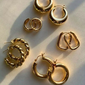 Assorted gold-toned stainless steel hoop earrings in various shapes and textures on white background