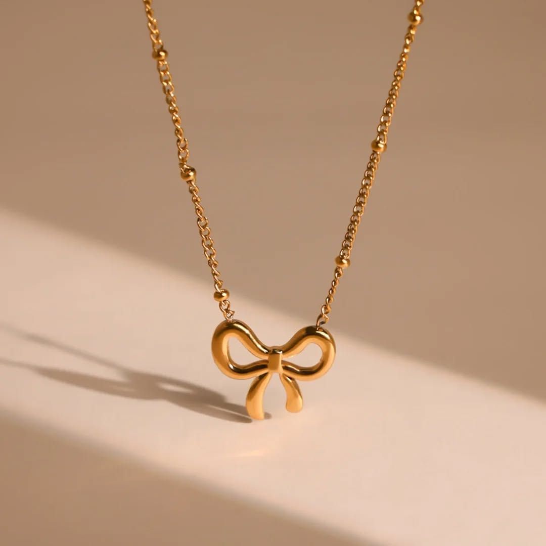 Gold stainless steel bow pendant necklace with delicate chain on neutral background