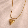 Gold heart pendant necklace on textured cream background, stainless steel jewelry for women