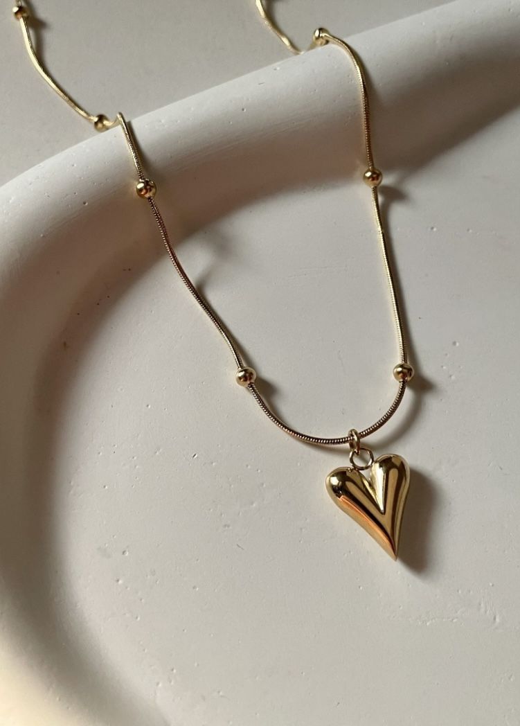Gold stainless steel necklace with heart pendant and bead accents on a neutral background