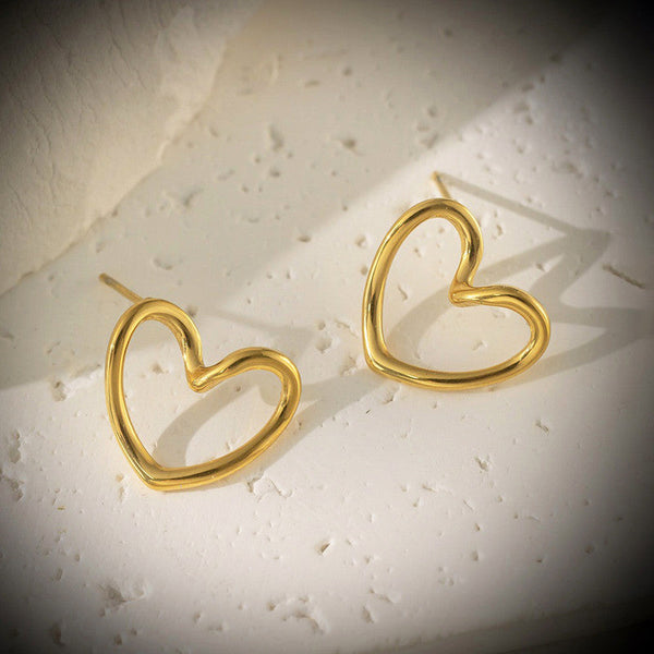 Gold heart-shaped open hoop stud earrings on a white textured surface