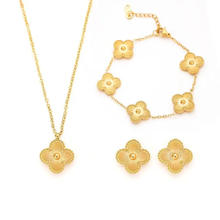 Gold stainless steel jewelry set with clover-shaped pendant, bracelet, and earrings on white background