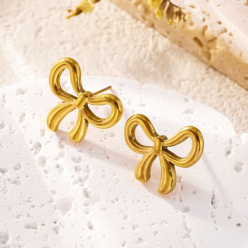 Gold stainless steel bow stud earrings on textured white stone surface